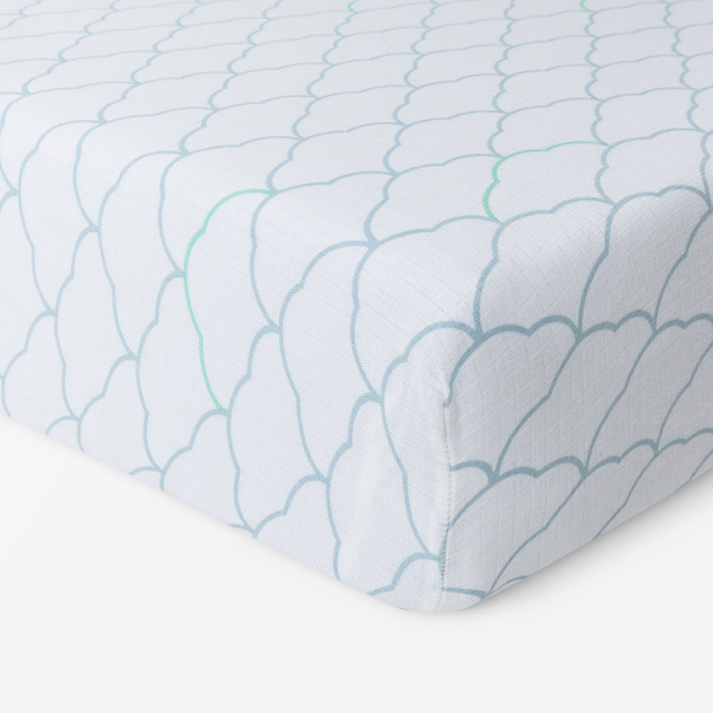 A close-up of Newton Baby Breathable, Organic Cotton Sheets (2-pack) on a mattress, showcasing a light blue scalloped pattern with green lines on white. Soft and hypoallergenic, the fabric neatly fits the corner—perfect for your baby’s crib.