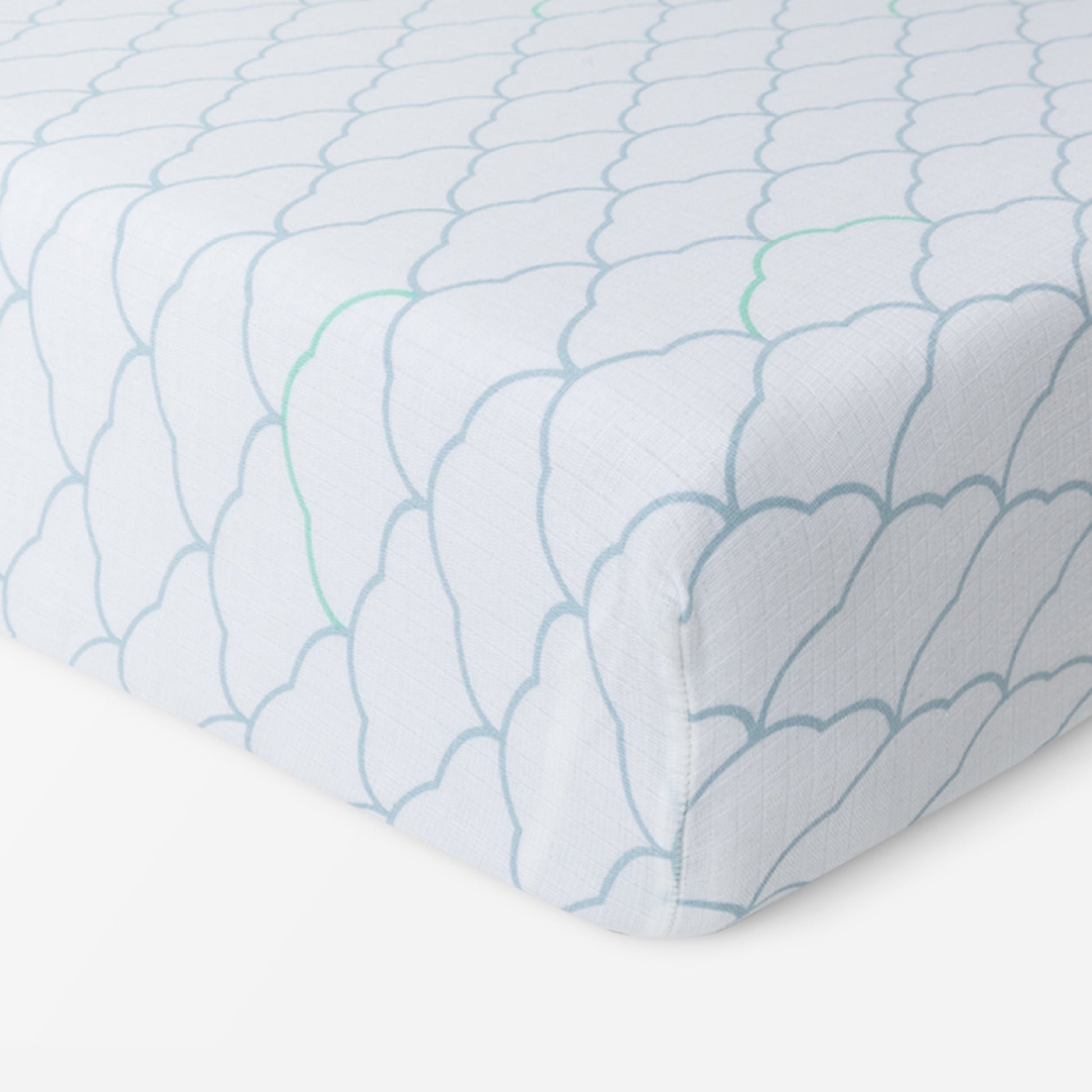 A close-up of Newton Baby Breathable, Organic Cotton Sheets (2-pack) on a mattress, showcasing a light blue scalloped pattern with green lines on white. Soft and hypoallergenic, the fabric neatly fits the corner—perfect for your baby’s crib.