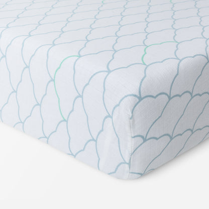 A close-up of Newton Baby Breathable, Organic Cotton Sheets (2-pack) on a mattress, showcasing a light blue scalloped pattern with green lines on white. Soft and hypoallergenic, the fabric neatly fits the corner—perfect for your baby’s crib.