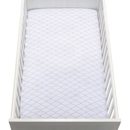 A white crib holds a mattress covered with a Newton Baby Breathable, Organic Cotton Sheet (2-pack) in white, featuring a subtle scalloped pattern. The photo is taken from above.