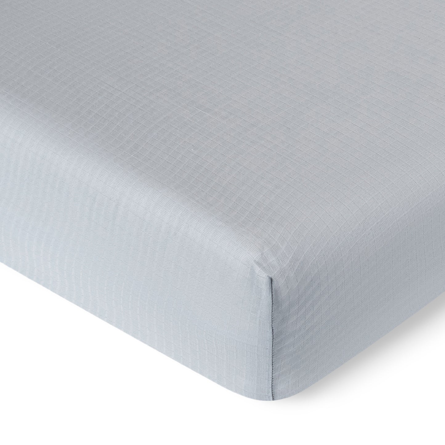 A close-up of the Newton Baby Breathable, Organic Cotton Sheets (2-pack) in light gray with a subtle checkered pattern, neatly fitted over the corner of a crib mattress.