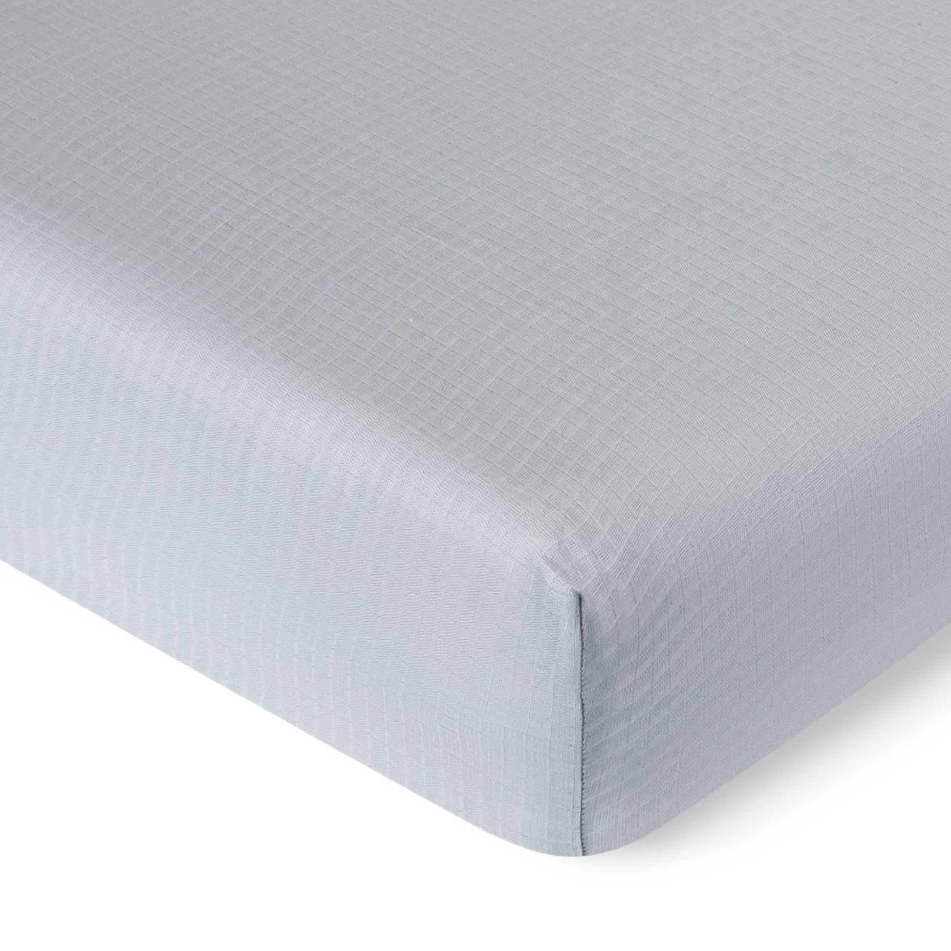 A close-up of the Newton Baby Breathable, Organic Cotton Sheets (2-pack) in light gray with a subtle checkered pattern, neatly fitted over the corner of a crib mattress.