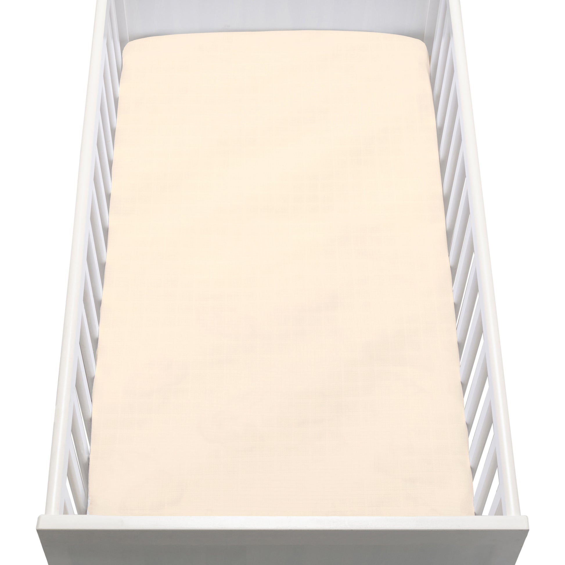 A white baby crib with vertical slats is shown from above, featuring a neatly made mattress covered with Newton Baby Breathable, Organic Cotton Sheets (2-pack) in pale cream. The crib is empty.