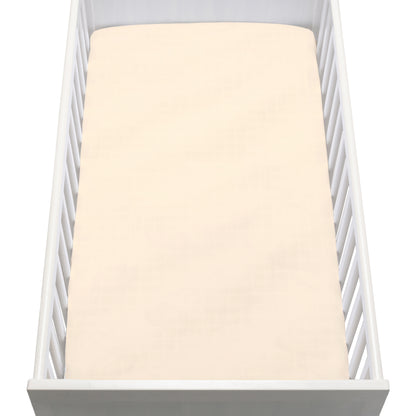 A white baby crib with vertical slats is shown from above, featuring a neatly made mattress covered with Newton Baby Breathable, Organic Cotton Sheets (2-pack) in pale cream. The crib is empty.