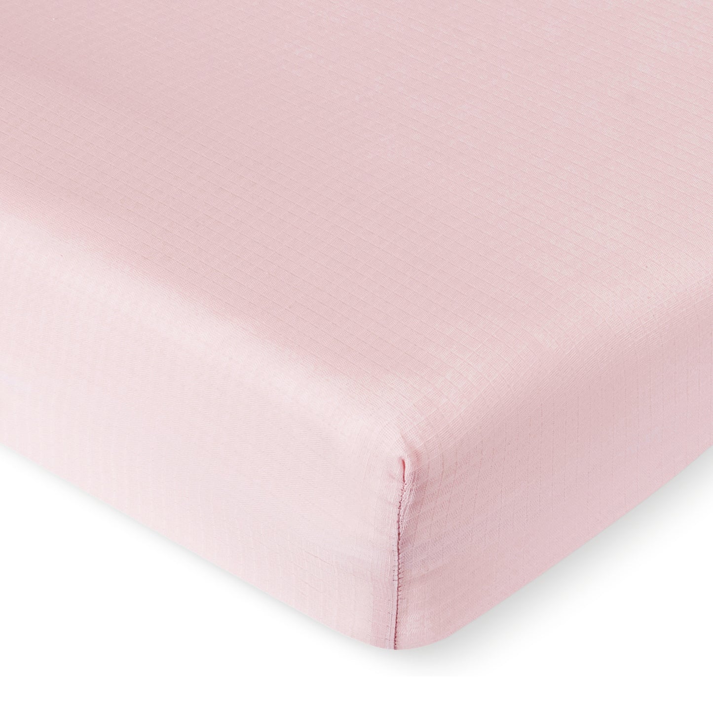A close-up of a Newton Baby Breathable, Organic Cotton Sheet (2-pack) in light pink neatly covering a mattress corner, highlighting the subtle grid texture on the fabric.