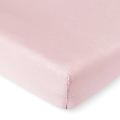 A close-up of a Newton Baby Breathable, Organic Cotton Sheet (2-pack) in light pink neatly covering a mattress corner, highlighting the subtle grid texture on the fabric.