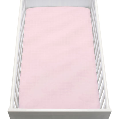 A white crib with vertical slats is seen from above, featuring a Newton Baby Breathable, Organic Cotton Sheet (2-pack) in pale pink, neatly fitted on the mattress.
