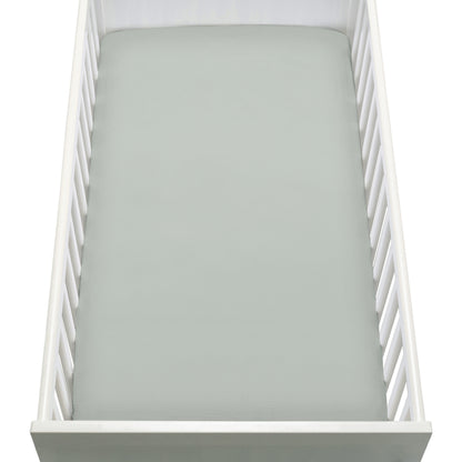 A top-down view of a white baby crib with a Newton Baby Breathable, Organic Cotton Sheet (2-pack) in light gray on the mattress. The crib has slatted sides and a solid end panel.