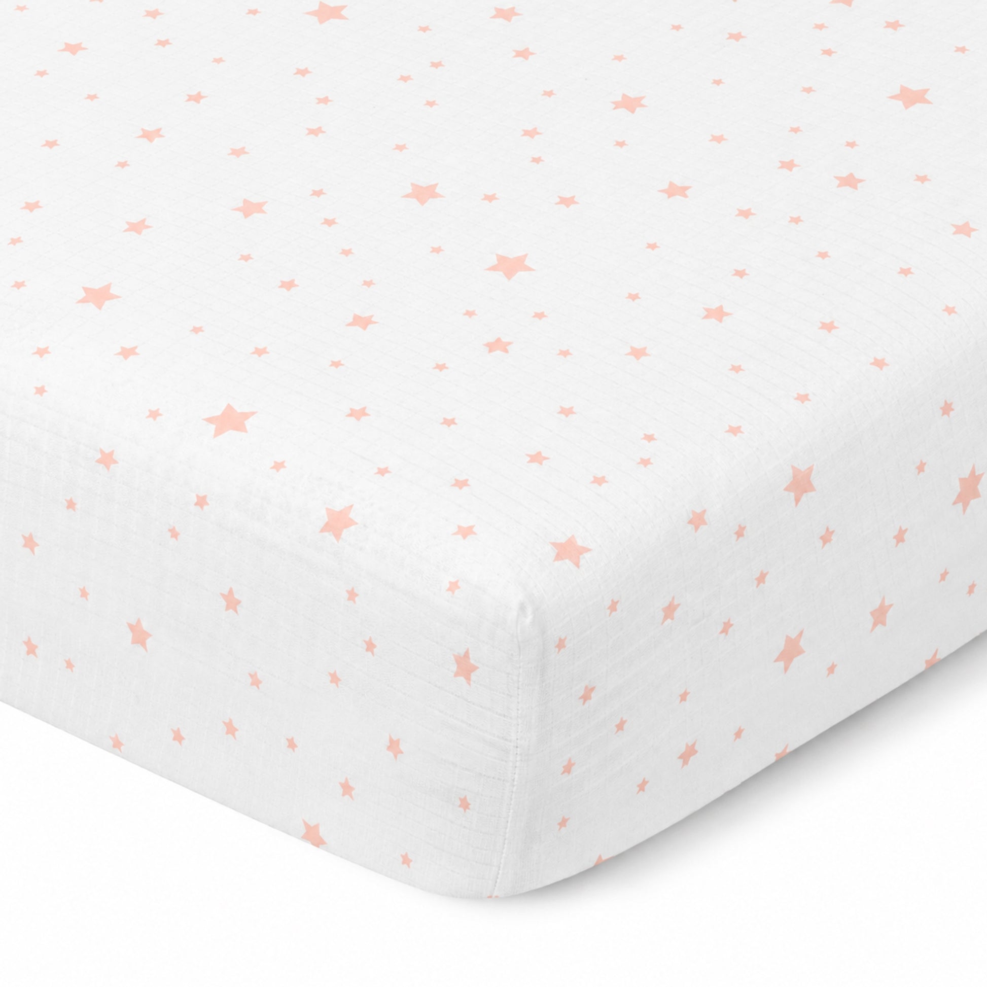 A close-up of Newton Baby's Breathable, Organic Cotton Sheets (2-pack) in white with pink stars, snugly fitted on a mattress. Made from breathable crib sheet material for added comfort.