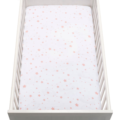 A white baby crib with a mattress covered in Newton Baby’s breathable, organic cotton sheet featuring pink and peach stars.