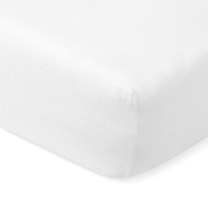 Close-up of a white, fitted Newton Baby Breathable, Organic Cotton Sheet (2-pack) with a subtle checkered pattern, tightly stretched over the corner of a crib mattress.