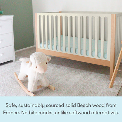 A modern nursery with the Newton Galileo Convertible Crib by Newton Baby, crafted from solid beech wood for safety and durability, plus a white rocking sheep toy. The crib includes a toddler bed conversion kit for growing families.