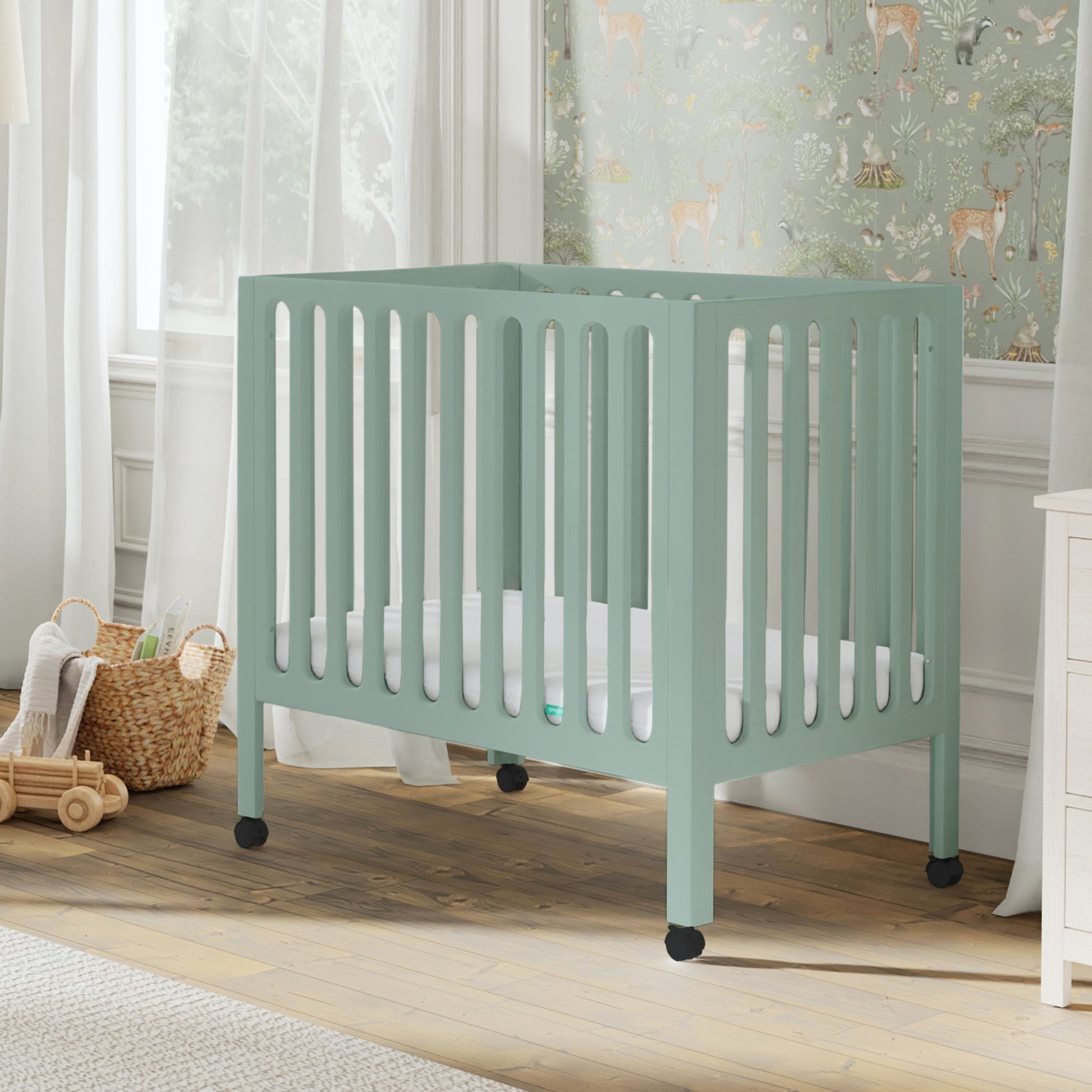 Green crib in a nursery with toys and a basket on the floor. 999-8430-SGE