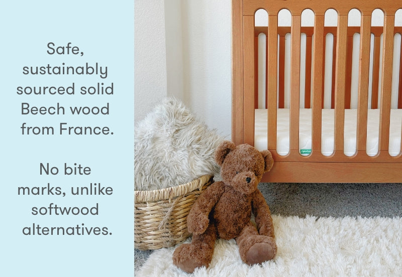 A plush teddy bear sitting beside a wooden crib with text overlay that reads "Safe, sustainably sourced solid Beech wood from France. No bite marks, unlike softwood alternatives."