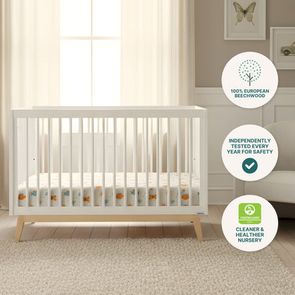 The Soho Convertible Crib by dadada baby features sturdy beechwood in a cozy nursery with cream curtains, beige armchair, rug, and wall art. Badges highlight beechwood construction, safety testing, and GREENGUARD certification.
