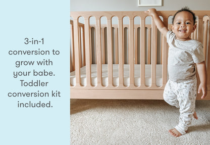 Happy toddler standing next to a crib with text '3-in-1 conversion to grow with your babe. Toddler conversion kit included.'