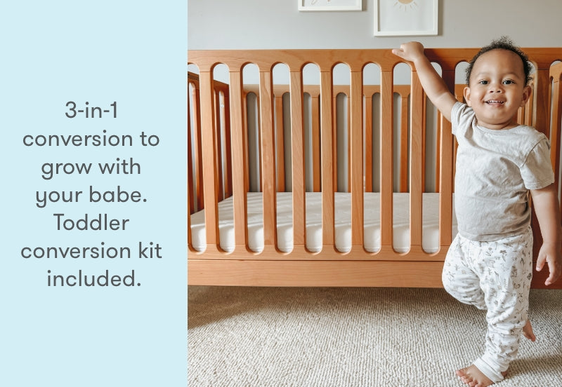 Toddler smiling next to a crib with text "3-in-1 conversion to grow with your babe. Toddler conversion kit included."