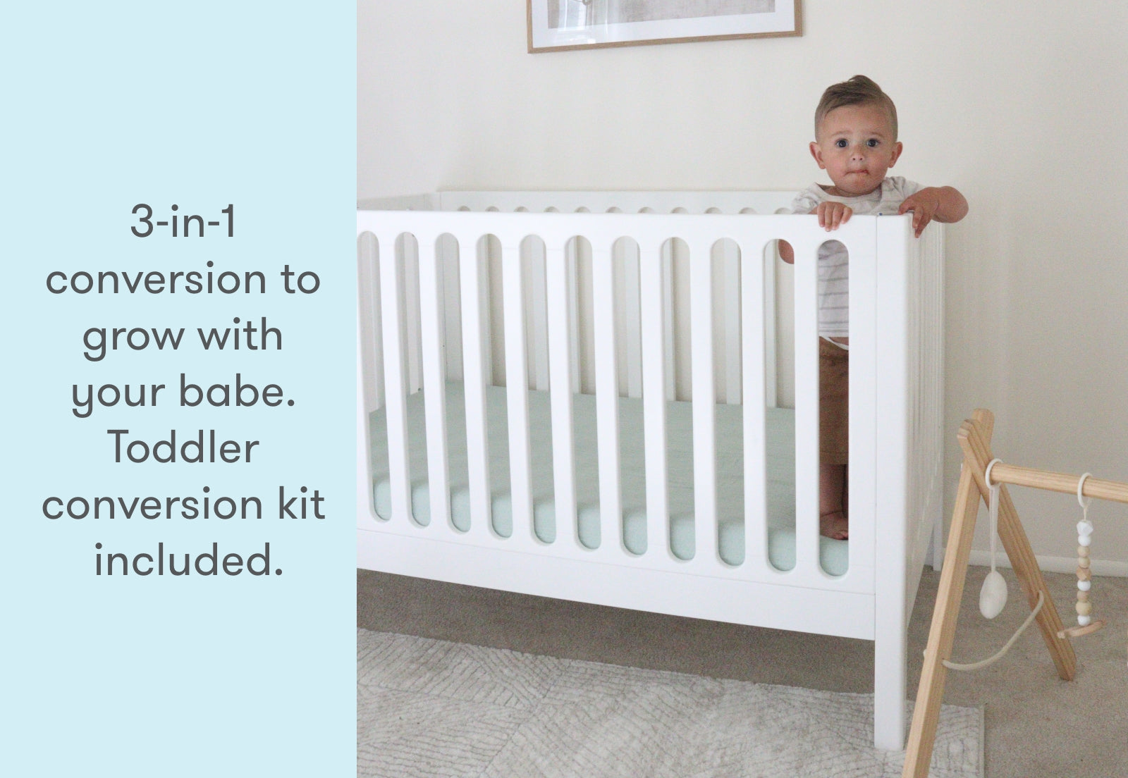 Toddler peeking over the side of a white 3-in-1 convertible crib, with text stating "3-in-1 conversion to grow with your babe. Toddler conversion kit included."