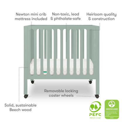 The Newton Galileo Mini Crib with Newton Mattress by Newton Baby is a pale green, solid beech wood crib with vertical slats, locking caster wheels for portability, and a white mattress. Made from non-toxic materials; PEFC and GREENGUARD certified.