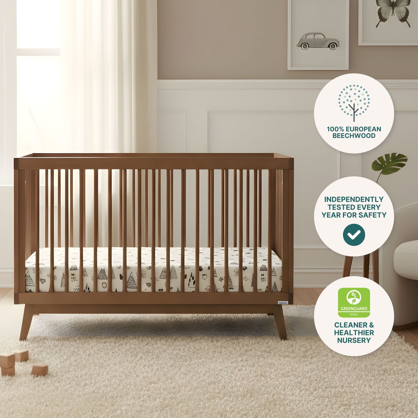 The dadada baby Soho Convertible Crib, crafted from European beechwood, is paired with a patterned Newton mattress in a softly lit nursery. Icons highlight its annual safety testing and GREENGUARD certification for healthier air.