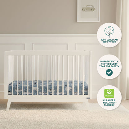 The softly lit nursery features the dadada baby Soho Convertible Crib—a white 3-in-1 design paired with a blue patterned Newton mattress. Badges highlight 100% European Beechwood, Greenguard certification, and safety testing. A car print hangs above.