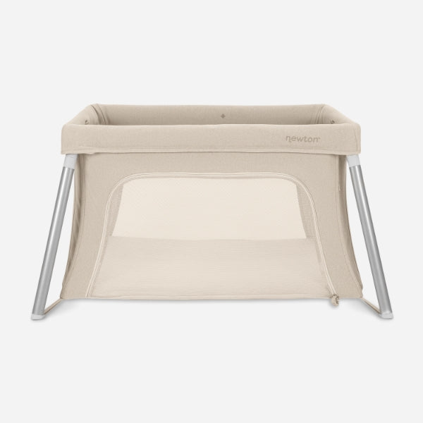 The Newton Baby Compact Travel Crib & Play Yard, shown on a white background, is beige with mesh sides, angled metal legs, a breathable mattress, a rectangular shape, and a zippered front opening.
