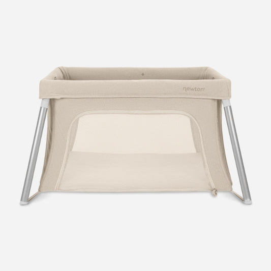 The Newton Baby Compact Travel Crib & Play Yard, shown on a white background, is beige with mesh sides, angled metal legs, a breathable mattress, a rectangular shape, and a zippered front opening.