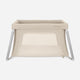The Newton Baby Compact Travel Crib & Play Yard, shown on a white background, is beige with mesh sides, angled metal legs, a breathable mattress, a rectangular shape, and a zippered front opening.