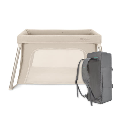The Newton Baby Compact Travel Crib & Play Yard is a beige portable crib with mesh sides and comes with a gray backpack for easy transport. Its compact design and included washable mattress offer convenient travel and storage.