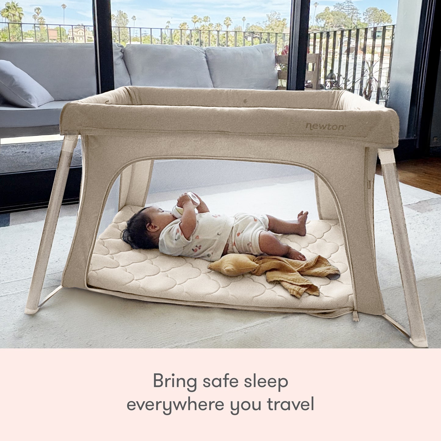 A baby rests in the Newton Baby Compact Travel Crib & Play Yard with breathable mesh sides, in a sunlit room. Text below: Ensure safe sleep anywhere with Newton Baby’s Compact Travel Crib & Play Yard.