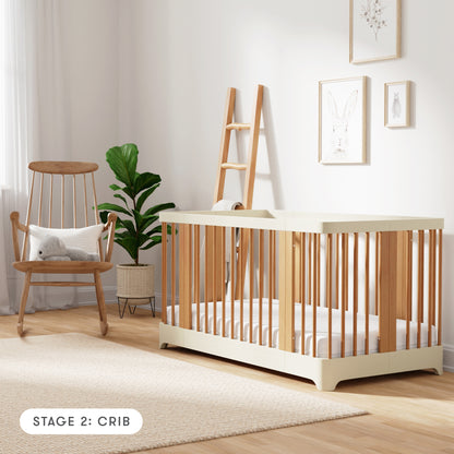 Natural + Dove White color Newton Nest Convertible Crib in crib setting, in nursery next to rocking chair, with text "Stage 2: Crib"