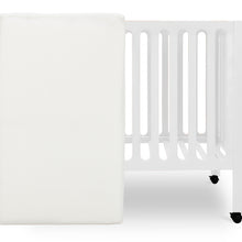 White crib mattress by a crib with slatted sides on a white background.