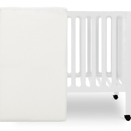 White crib mattress by a crib with slatted sides on a white background. skip