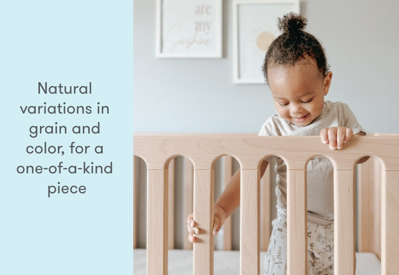 Toddler smiling while holding onto a wooden crib with the text "Natural variations in grain and color, for a one-of-a-kind piece."