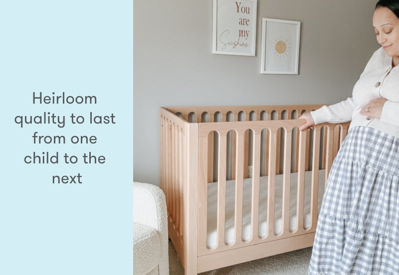 A pregnant woman in a white sweater and checked skirt smiles down at a sturdy, wooden crib in a nursery, with the text "Heirloom quality to last from one child to the next" displayed on the image.