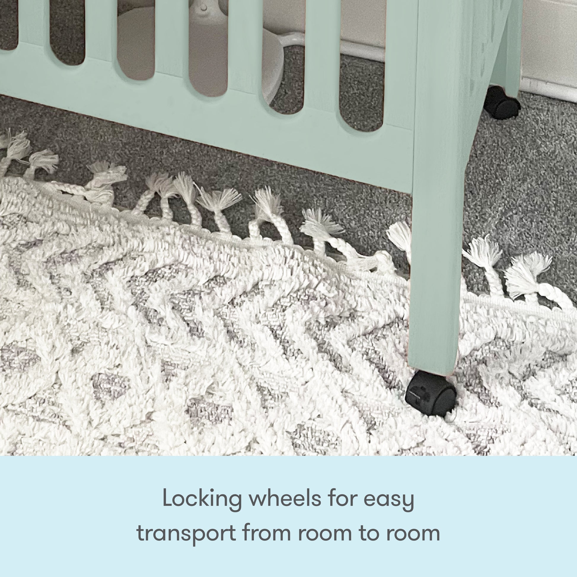 A close-up of a Newton Baby Galileo Mini Crib with Newton Mattress leg shows the black locking wheel on a textured white rug, emphasizing the mobility feature. Text: Locking wheels let you easily move the crib from room to room.