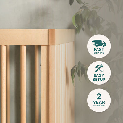 Close-up of the dadada baby Soho Convertible Crib in mid-century style, with green leaves behind it. Three icons to the right say: “Fast Shipping,” “Easy Setup,” and “2 Year Warranty.”.