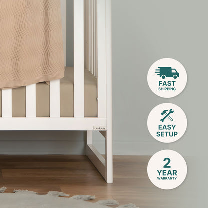 The Austin Convertible Crib by dadada baby, shown with beige bedding and a Newton crib mattress on a sustainable beechwood floor. Three icons indicate: Fast Shipping, Easy Setup, and 2 Year Warranty.