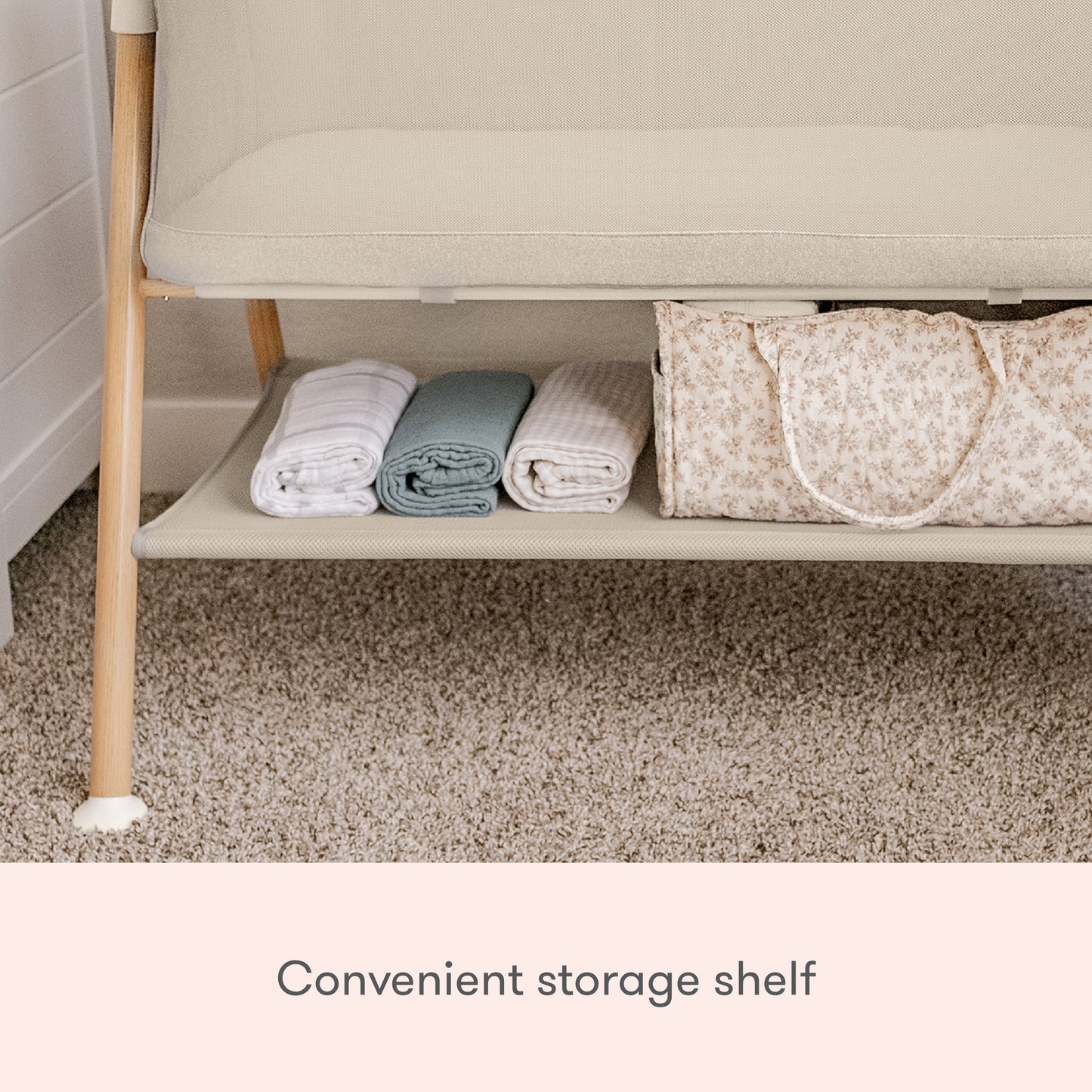 A close-up of the lower shelf on the Newton Baby Essential Bassinet shows folded blankets, towels, and a patterned storage bag neatly organized. Text reads: Convenient storage shelf.