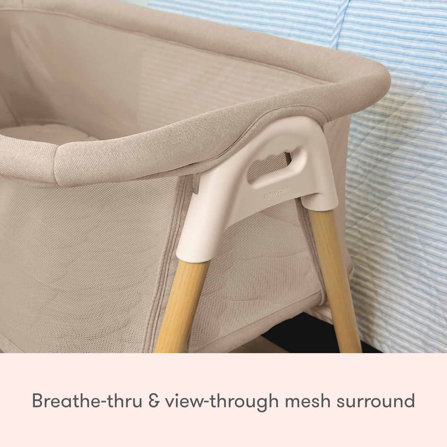A close-up of the Newton Baby Essential Bassinet, featuring breathable, view-through mesh sides and wooden legs, is placed next to a blue-striped surface.