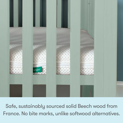 A close-up of the Newton Galileo Mini Crib with Newton Mattress by Newton Baby, featuring light green sustainably sourced French Beech wood, a white mattress inside, portability, and bite mark resistance for your baby’s safety.