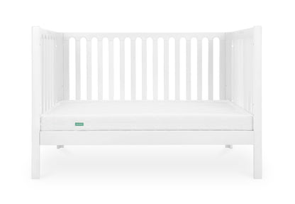 A simple white baby crib with a clean mattress displaying a small green 'Newton' logo on its corner.