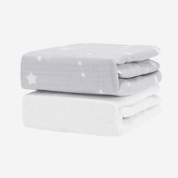 The Newton Baby Breathable, Organic Cotton Sheets (2-pack) includes one light gray sheet with white stars and one plain white sheet, both folded and set against a white background.