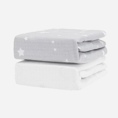The Newton Baby Breathable, Organic Cotton Sheets (2-pack) includes one light gray sheet with white stars and one plain white sheet, both folded and set against a white background.
