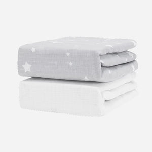 The Newton Baby Breathable, Organic Cotton Sheets (2-pack) includes one light gray sheet with white stars and one plain white sheet, both folded and set against a white background.