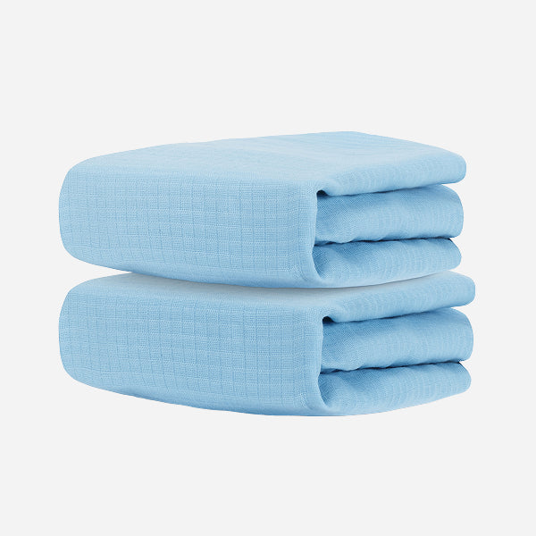 Two neatly folded, light blue Newton Baby Breathable, Organic Cotton Sheets (2-pack) stacked against a plain white background, evoking the softness and purity of hypoallergenic nursery essentials.