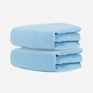 Two neatly folded, light blue Newton Baby Breathable, Organic Cotton Sheets (2-pack) stacked against a plain white background, evoking the softness and purity of hypoallergenic nursery essentials.