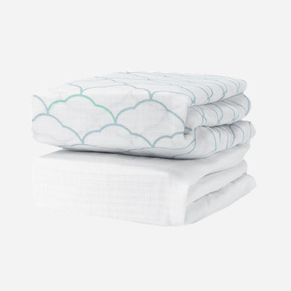 Newton Baby Breathable, Organic Cotton Sheets (2-pack): one features a light blue and green scallop design, the other is plain white. Both hypoallergenic crib sheets are shown folded on a white background for a crisp, clean look. 