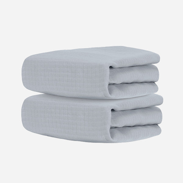 Two neatly folded light gray towels, stacked together against a white background, evoke the softness and comfort of Newton Baby's Breathable, Organic Cotton Sheets (2-pack).