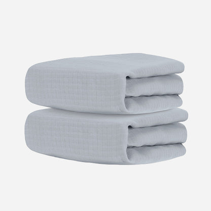 Two neatly folded light gray towels, stacked together against a white background, evoke the softness and comfort of Newton Baby's Breathable, Organic Cotton Sheets (2-pack).